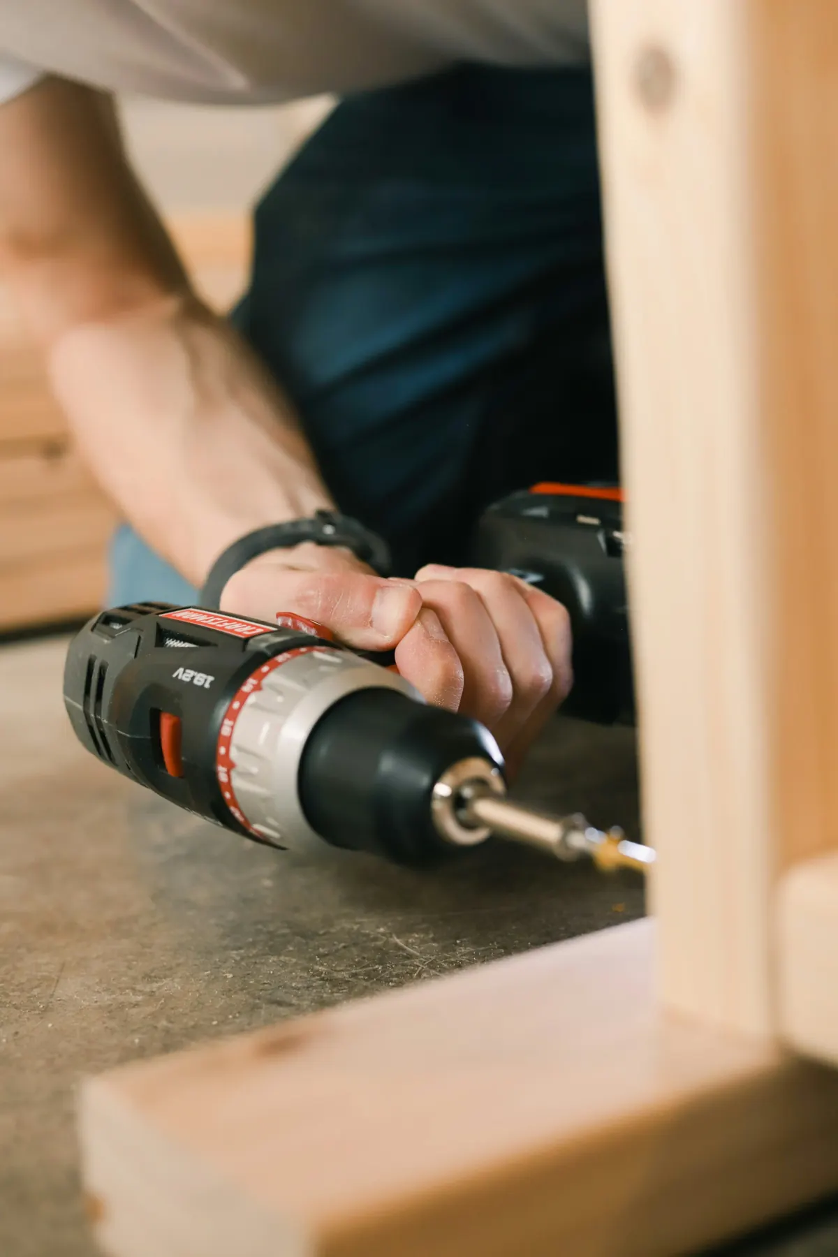 Hands drilling into a wood board with a cordless drill