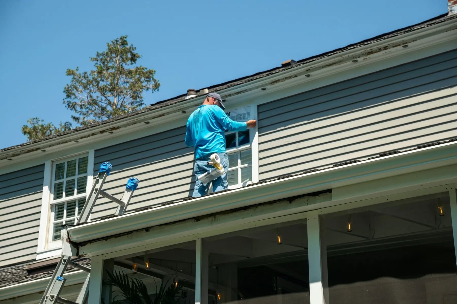 Contractor on a ladder installing flashing on the side of a grey house