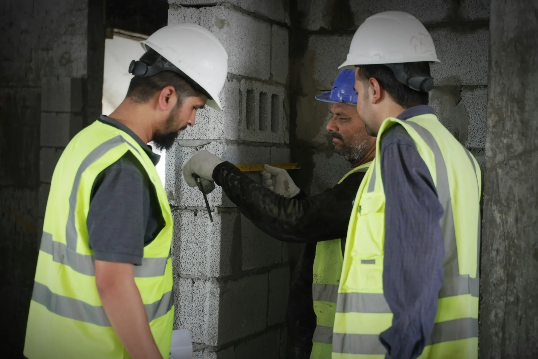 Three construction workers in high-visibility vests measuring on a job site